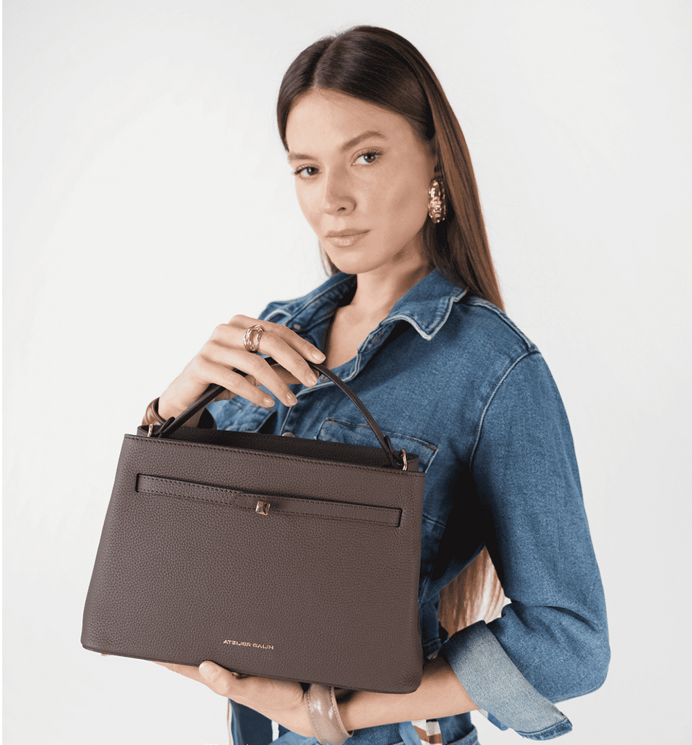 Woman holding a brown leather bag against a white background