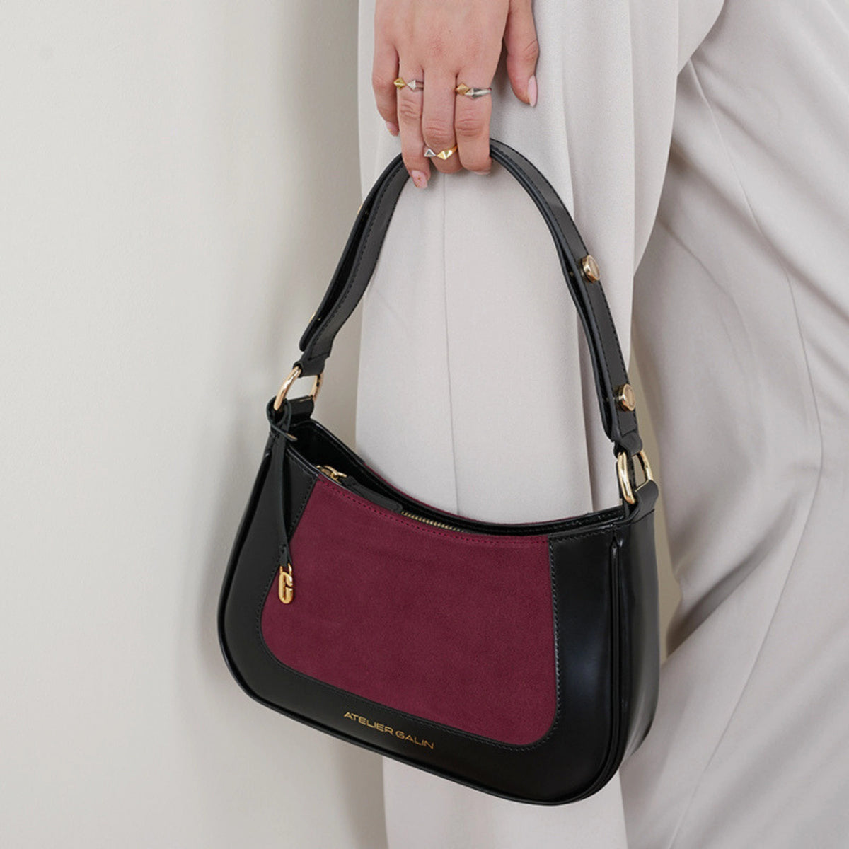 Black and burgundy handbag held by a person wearing a white outfit.