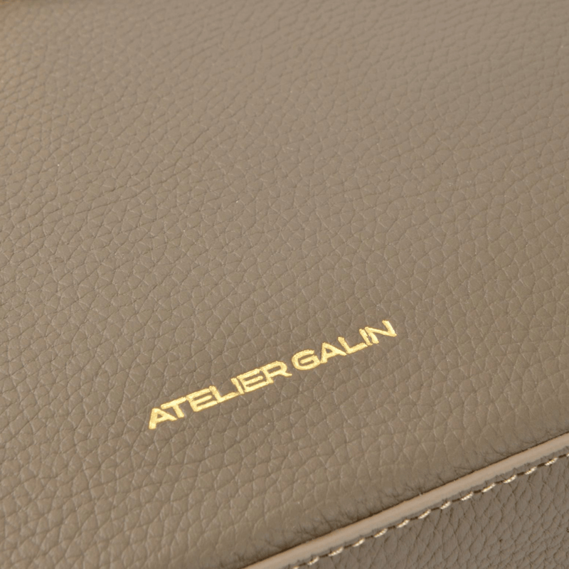 Close-up of a beige leather handbag with 'Atelier Galin' branding.