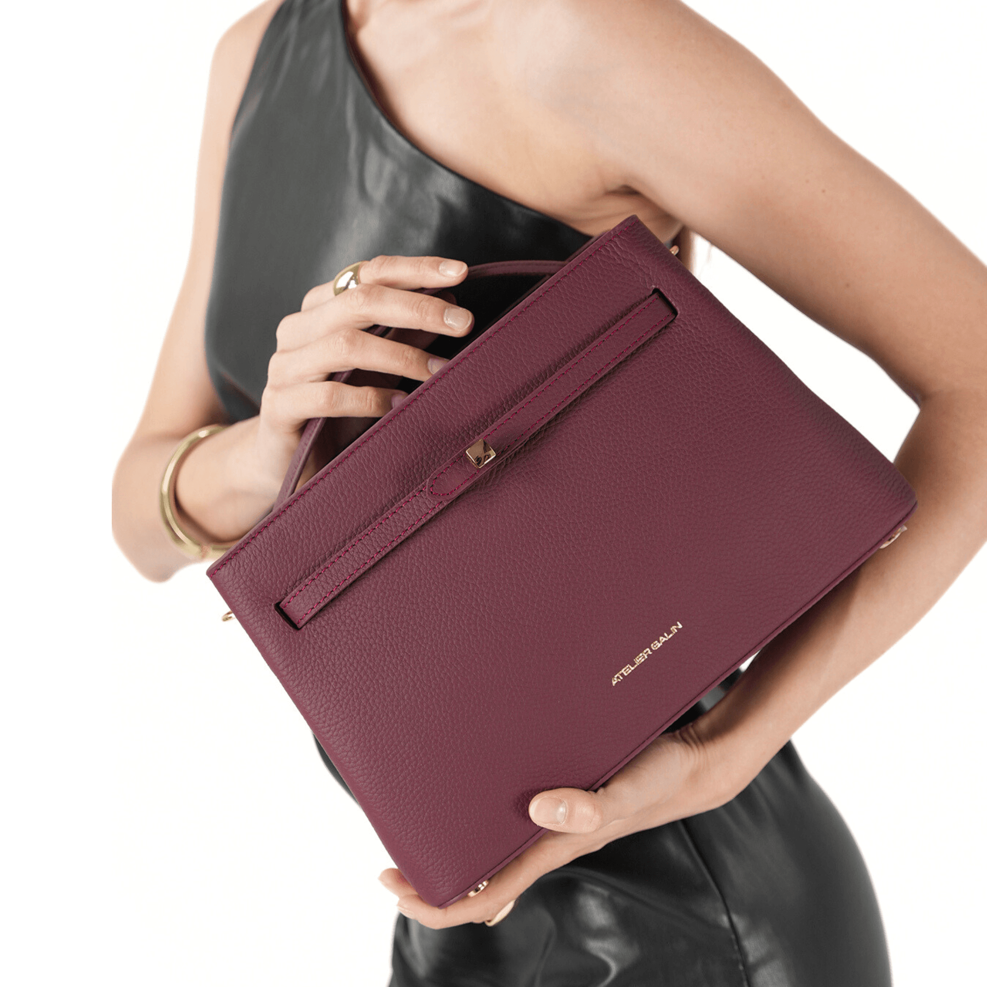 Person holding a burgundy atelier galin cube lock bag with atelier galin brand logo