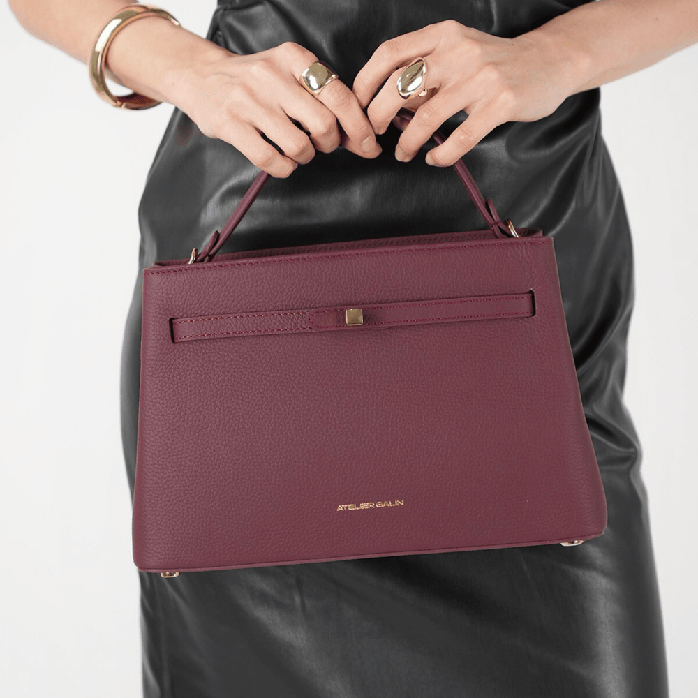 burgundy atelier galin cube lock handbag held by a person wearing a black leather outfit 