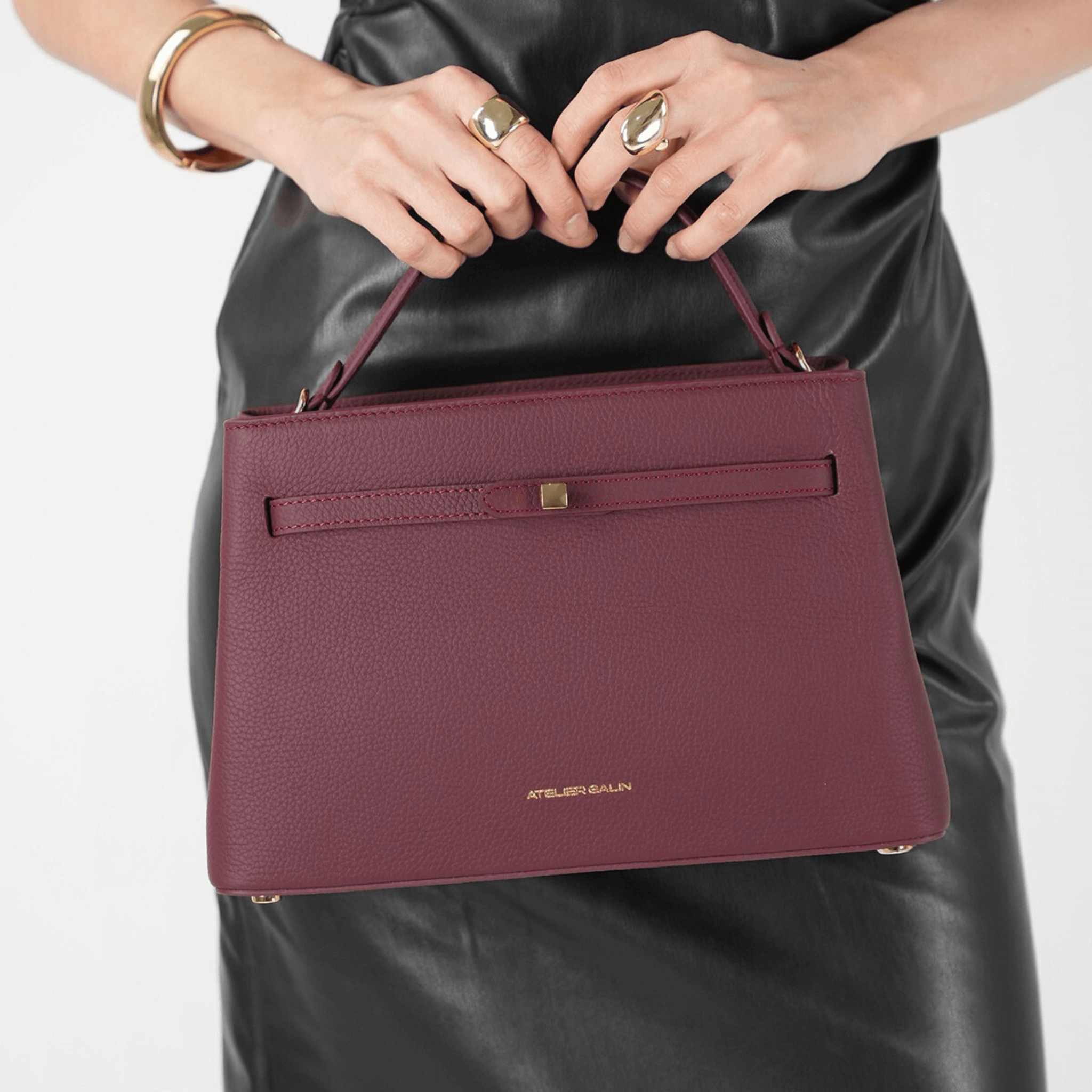 burgundy atelier galin cube lock handbag held by a person wearing a black leather outfit 