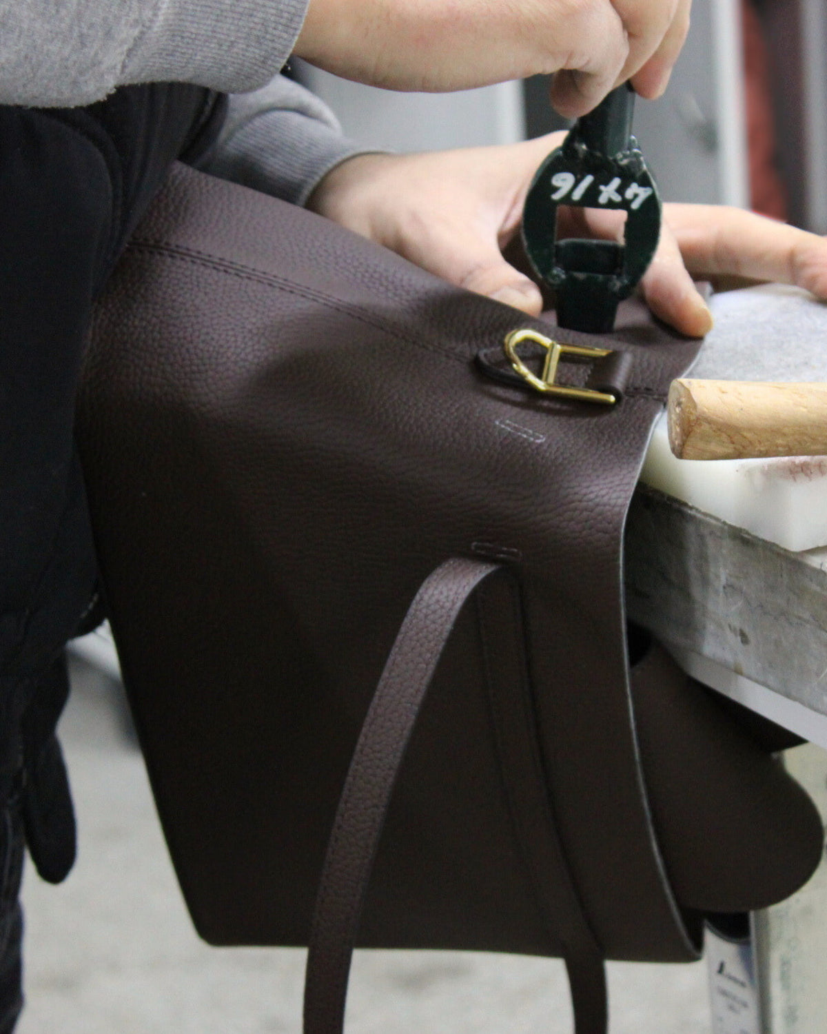 Person using a tool on a brown leather bag with a gold buckle.
