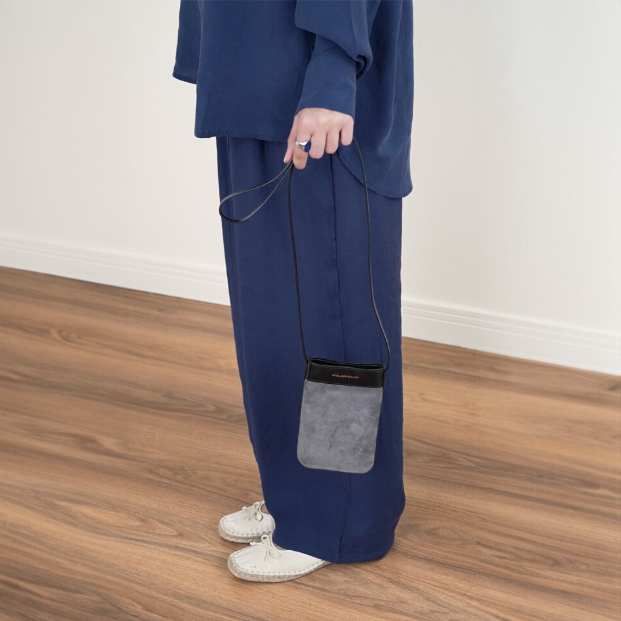 Person wearing a blue outfit with a gray suede phone bag on a wooden floor.