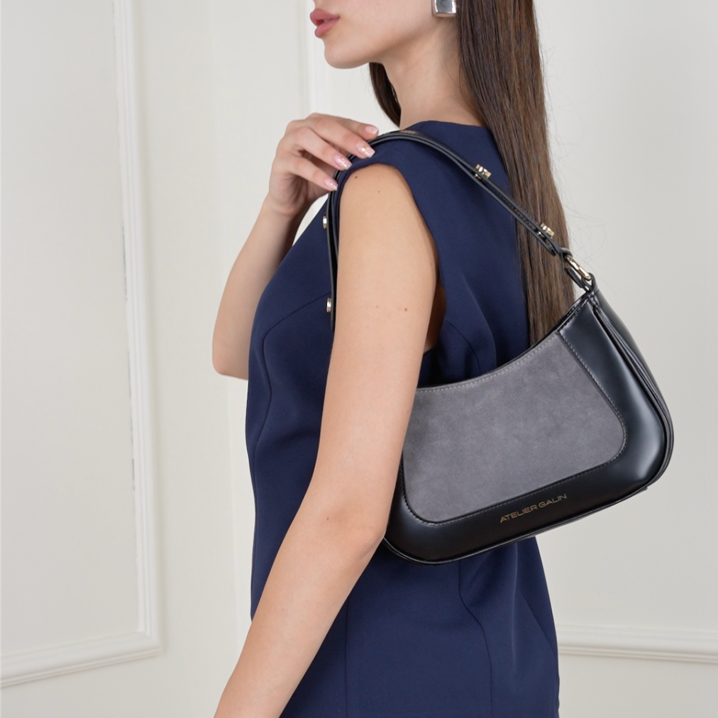 Woman in a navy outfit holding a black leather gray suede handbag against a white background