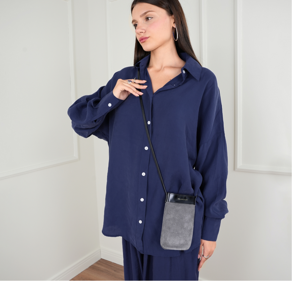 Woman wearing a blue outfit with a gray purse against a white paneled wall.