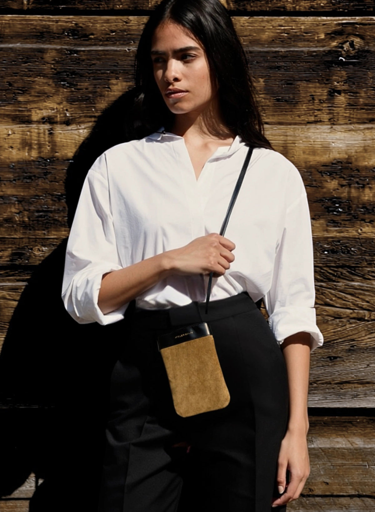 Woman holding a TABAC suede phone bag by atelier galin leather bag against a wooden background