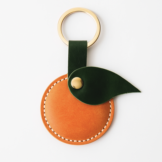 Leather orange keychain with green leaf and gold accent on a white background