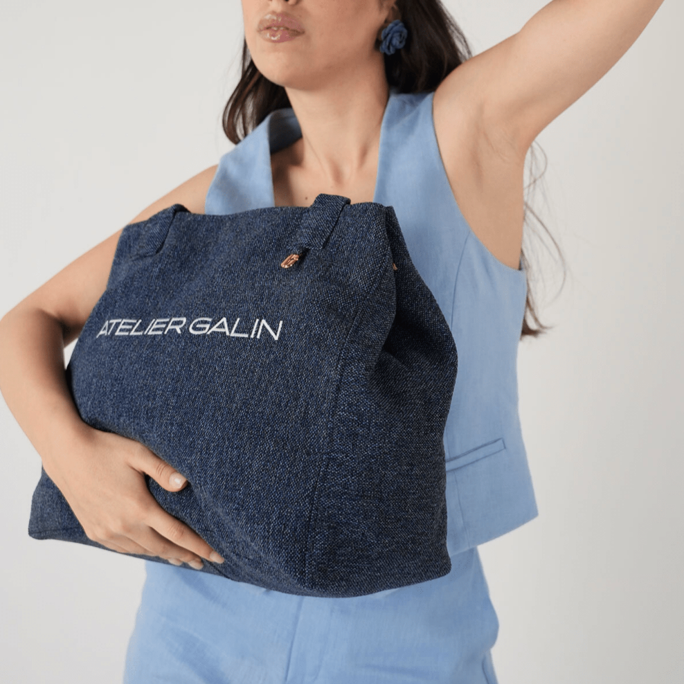 Woman holding a blue bag with 'Atelier Galin' branding against a white background